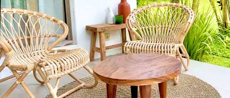 A wicker chair and table set on a woven mat, with a small wooden table beside them.