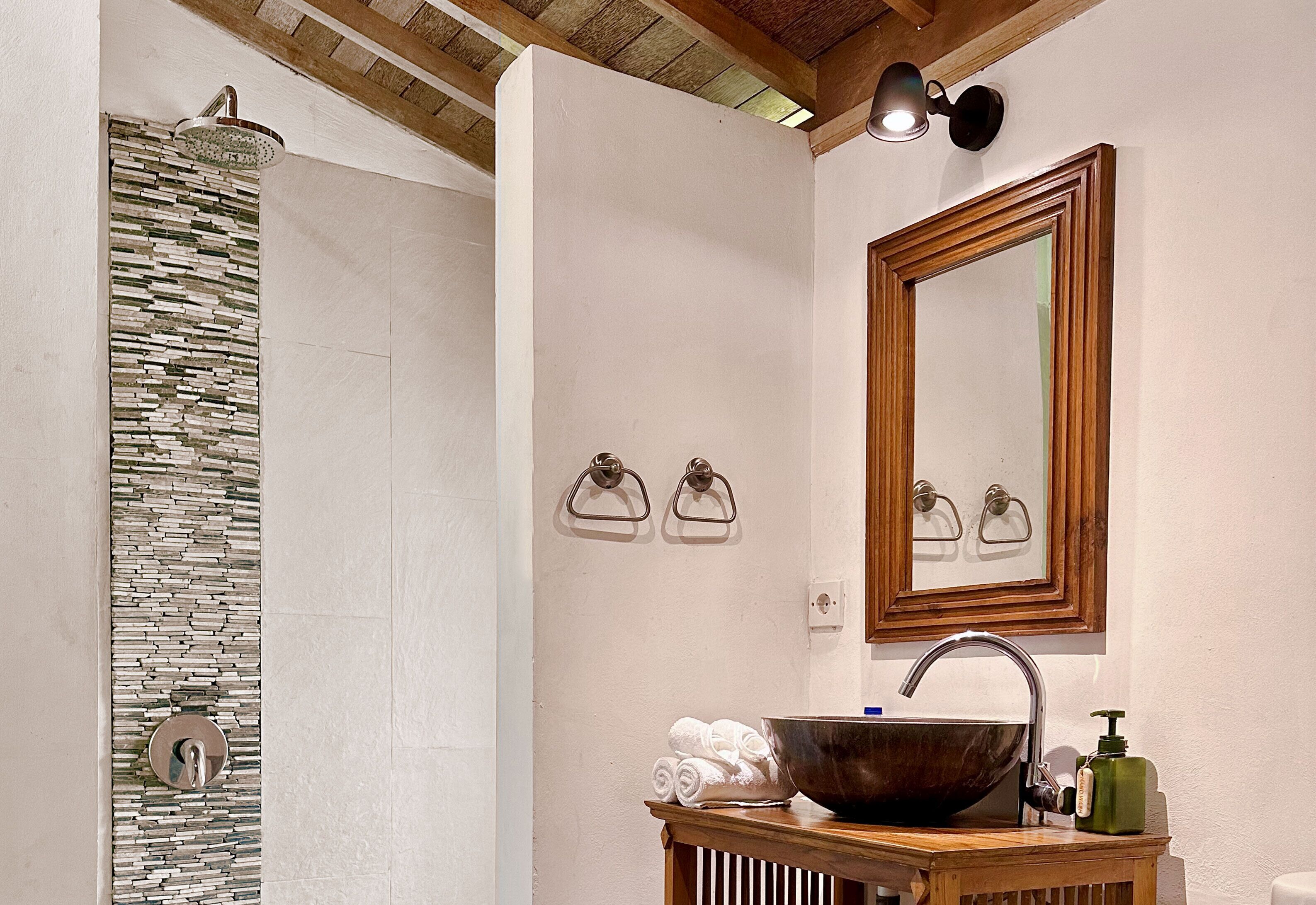 A bathroom with a stone shower wall, a wooden vanity with a large bowl sink, and a mirror above the sink.