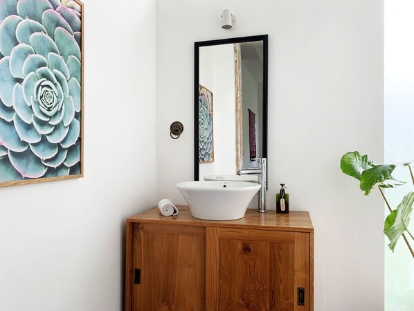 A bathroom with a wooden vanity, white sink, and a large mirror. - The White Villas Ubud (Ubud)