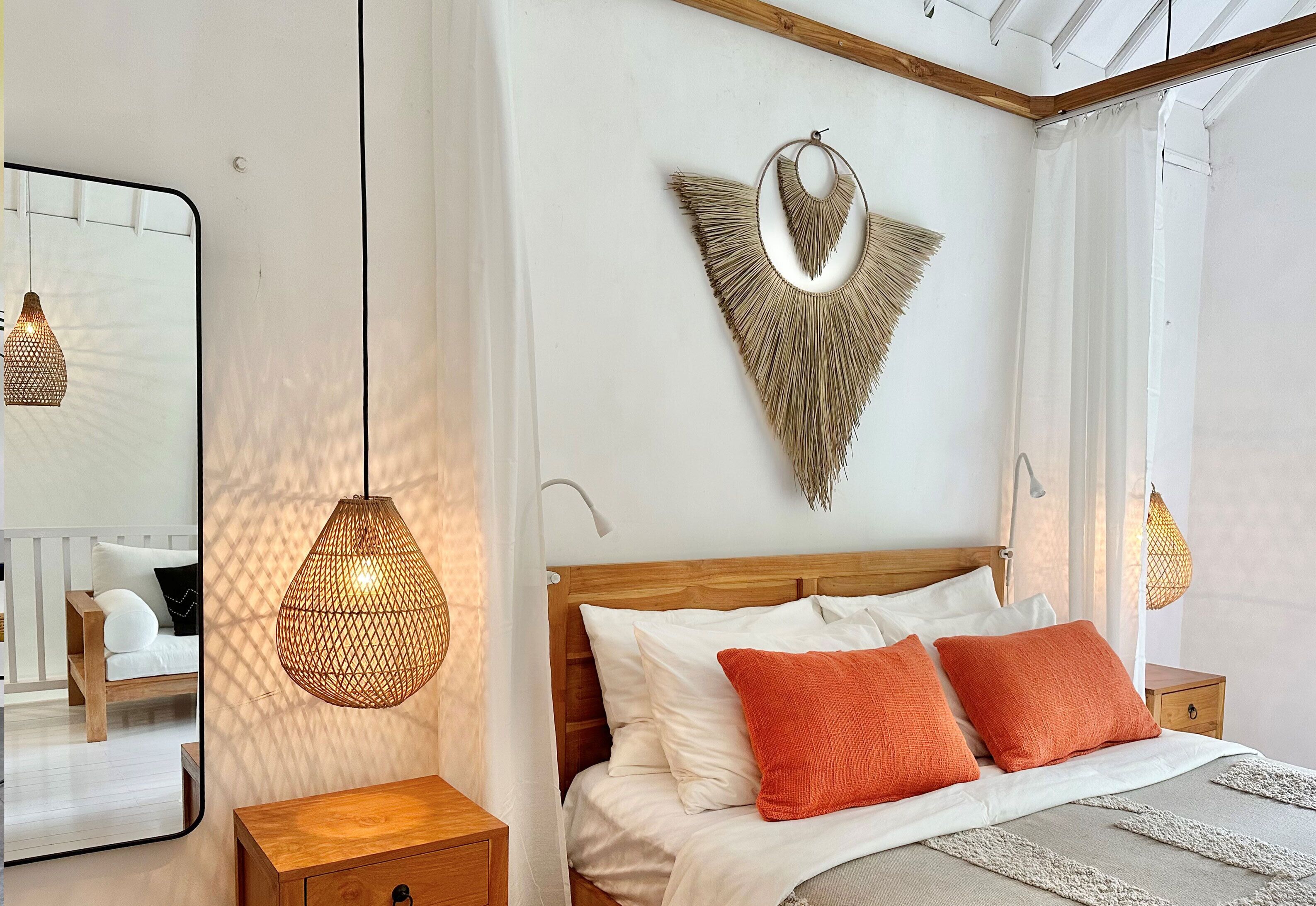 A bedroom with a wooden headboard, white bedding, and two orange pillows.