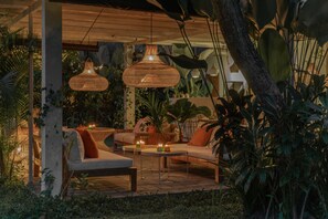 An outdoor seating area with wicker pendant lights, cushioned sofas, and a small table with candles. - The White Villas Ubud (Ubud)