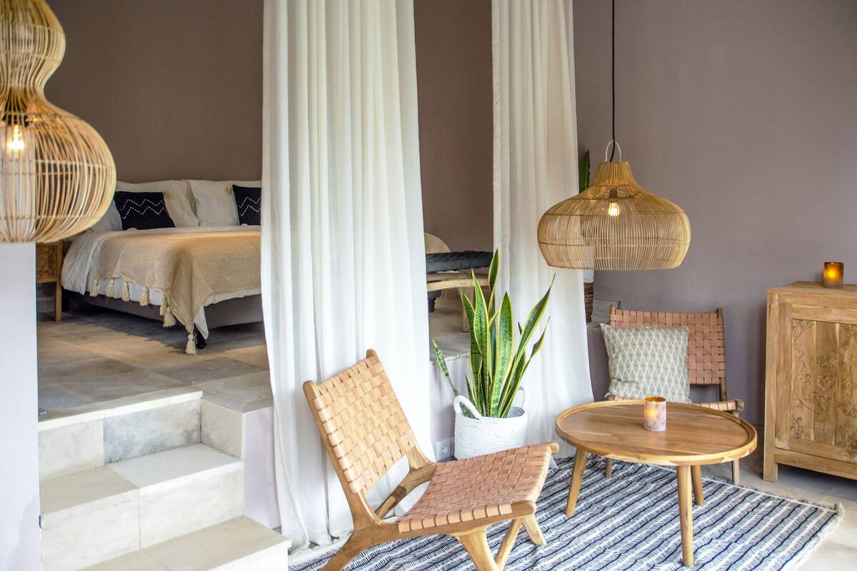 A bedroom with a bed, a chair, a table, and a potted plant.