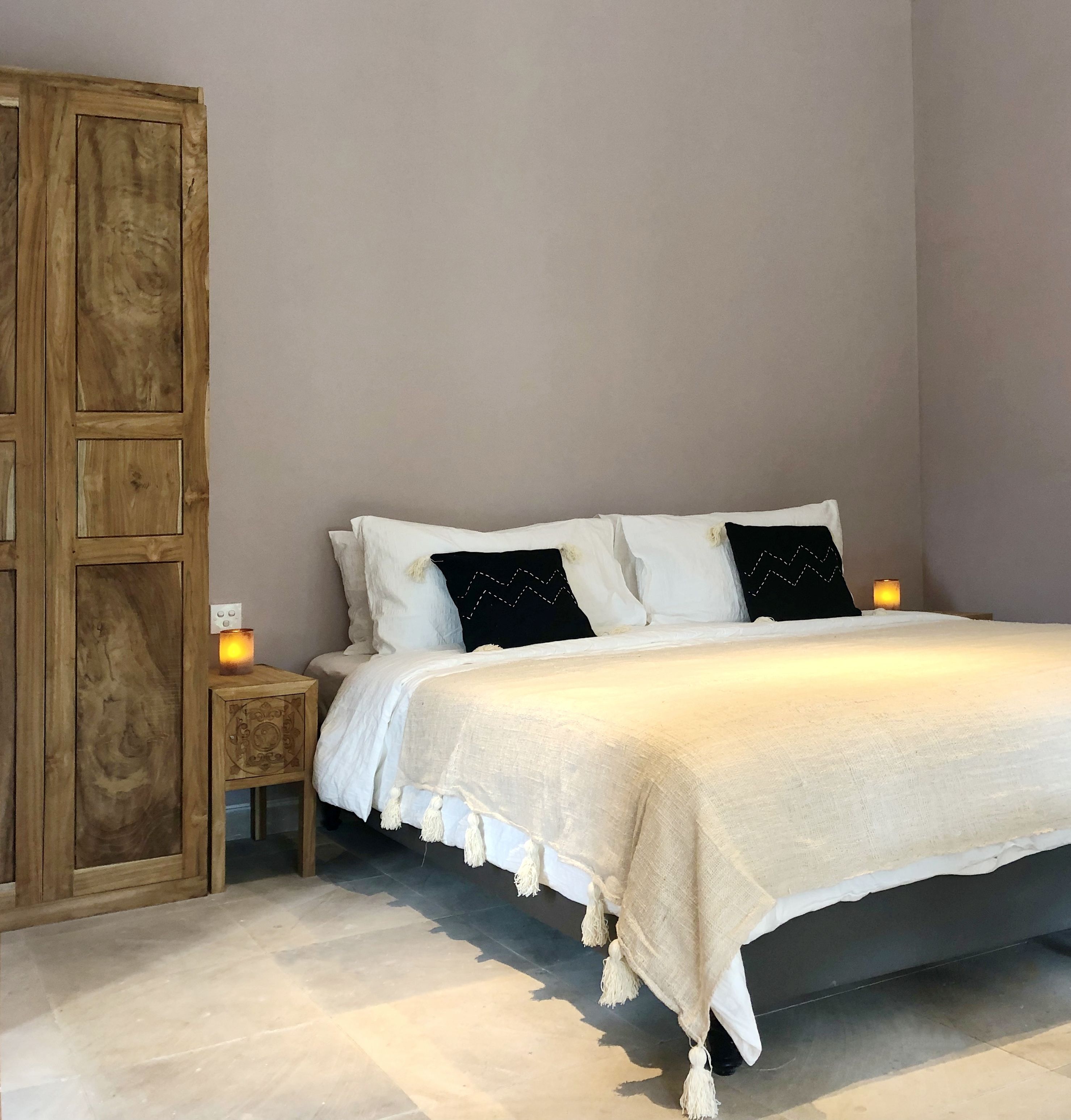 Un dormitorio con cama, mesitas de noche, un armario de madera y una lámpara fijada a la pared.