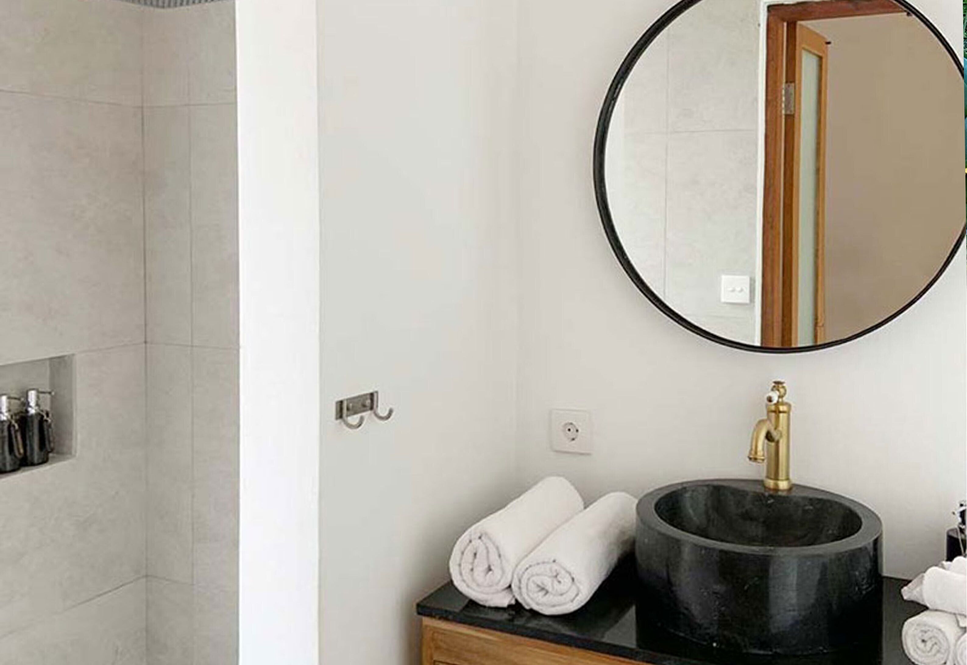 A bathroom with a round mirror, a black sink, and a shower area.