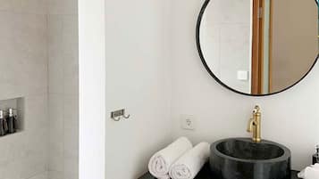 Une salle de bain avec un miroir rond, un lavabo noir et un espace douche.