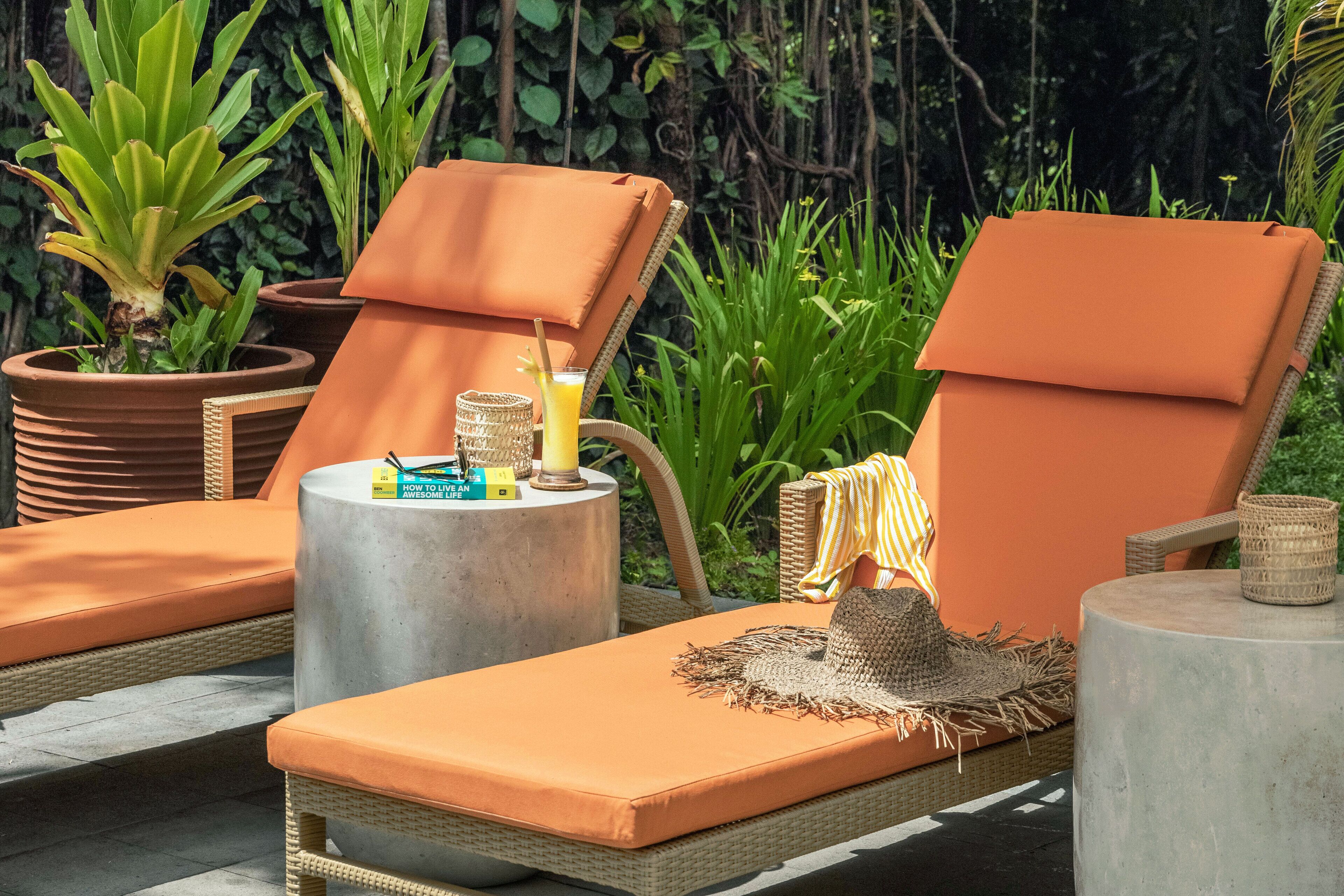 A sun lounge with wicker furniture, orange cushions, and a small table with a drink and a candle.