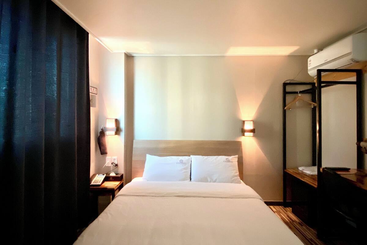 A hotel room with a large bed, a bedside table with a lamp, a hanging coat rack, and a mirror.