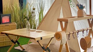 A cozy indoor camping setup with a teepee, a wooden table, and a fireplace. - Stay Pohang Hotel (Pohang)