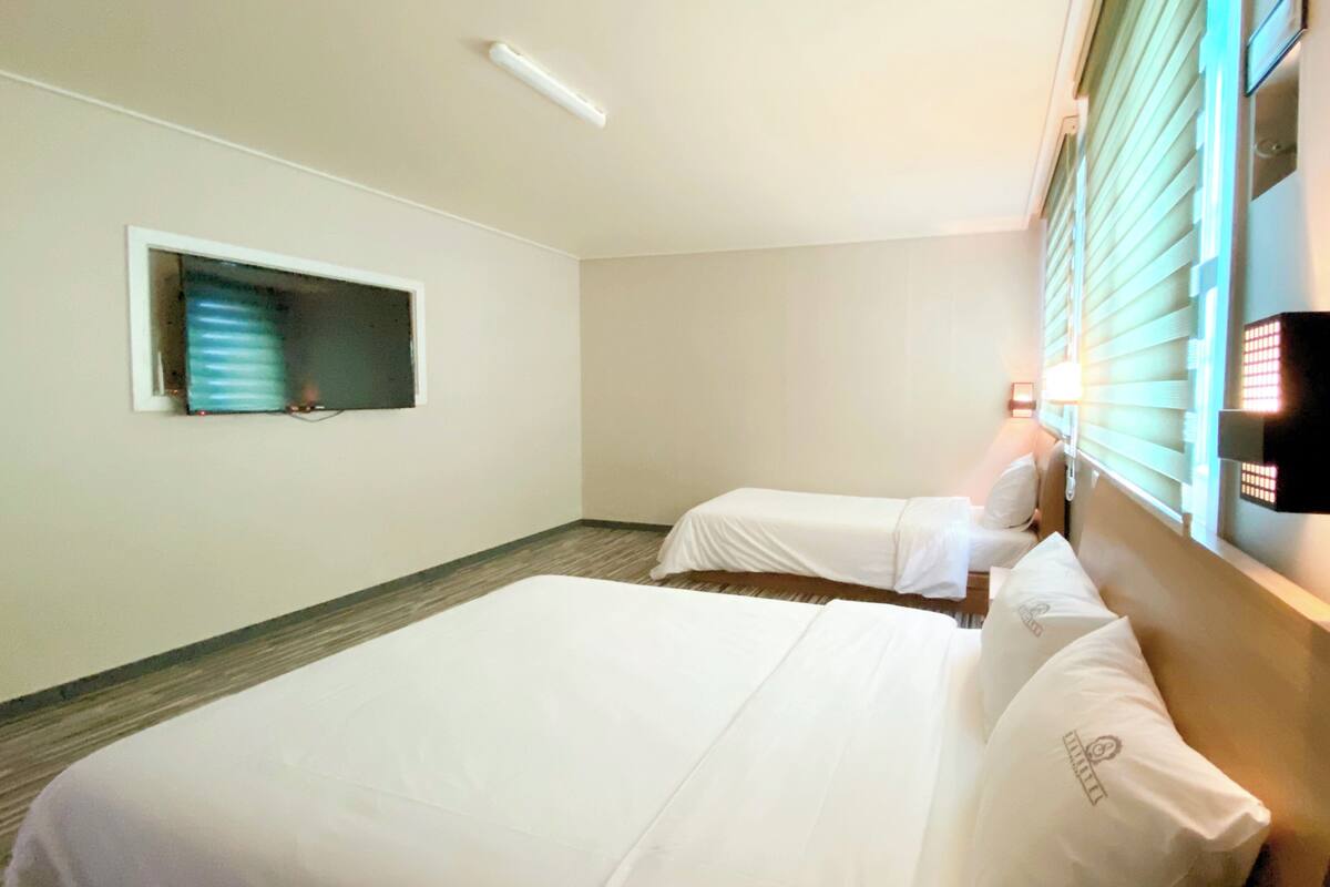 A hotel room with two beds, a small window, and a wall-mounted phone.
