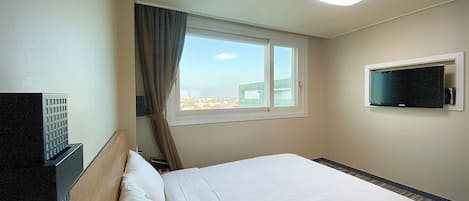 A hotel room with a bed, a television mounted on the wall, a window with curtains, and a ceiling light.