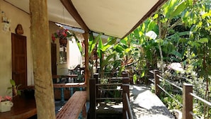 Uma área de pátio ao ar livre com um banco de madeira, uma cesta de flores suspensa e um portão de metal.