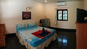 Quarto com cama, uma cadeira de madeira, televisão e janela com cortinas.