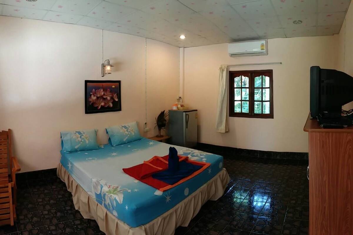 A bedroom with a bed, a wooden chair, a television, and a window with curtains.
