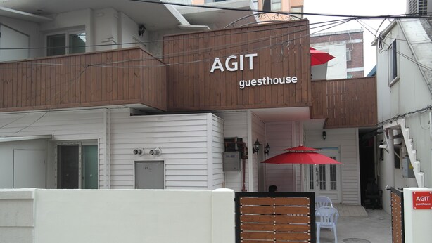 A guesthouse named AGIT with a wooden facade, white exterior walls, and a red umbrella. - Agit Guesthouse (Seoul)