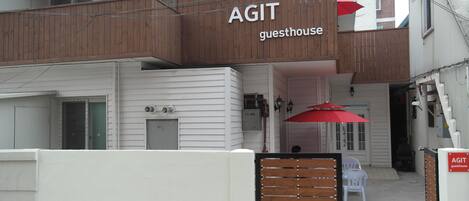 A guesthouse named AGIT with a wooden facade, white exterior walls, and a red umbrella.