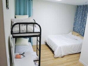 A dormitory room with bunk beds, a single bed, a small table with a phone, and a curtain.