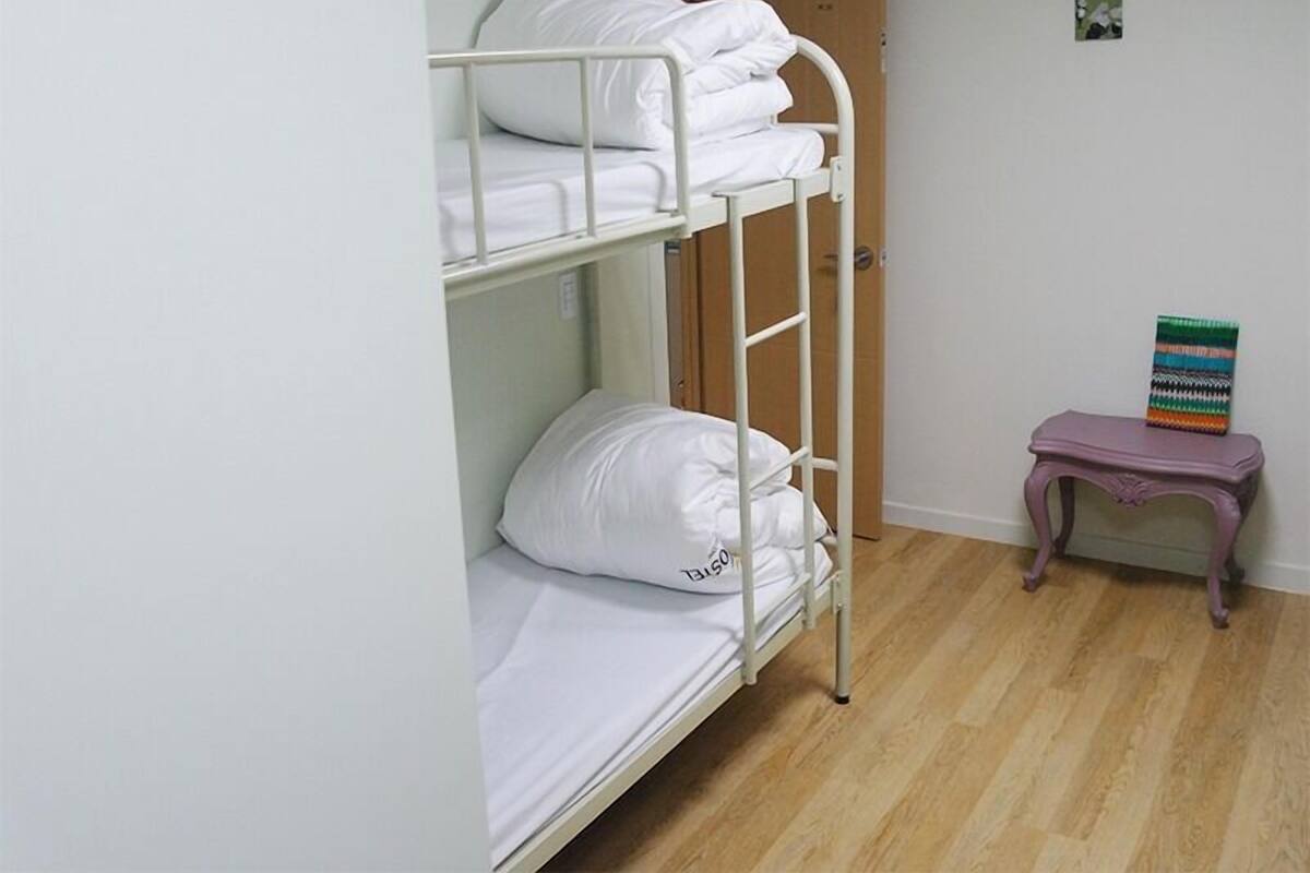 A bunk bed room with white bedding, a wooden door, and a small purple table with a colorful mat.