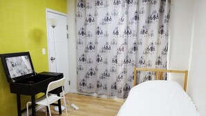 A room with a bed, a desk with a chair, a door, and a curtain with a pattern. - Agit Guesthouse (Seoul)