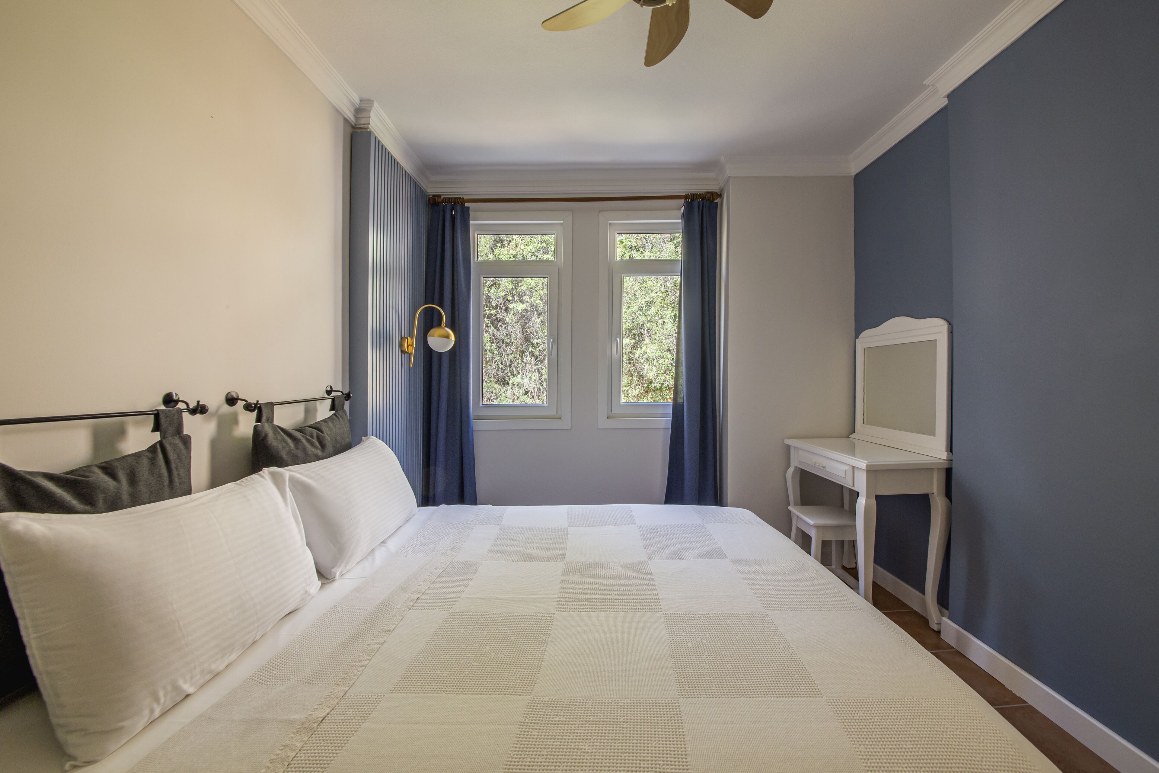A bedroom with a bed, a desk, and a window with curtains.