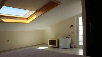 Een slaapkamer met dakraam, een bed, een klein wit kastje en een deur naar een andere kamer.