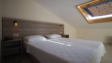 A bedroom with a wooden headboard, a single bed with white bedding, two bedside tables, and a skylight with a floral view.