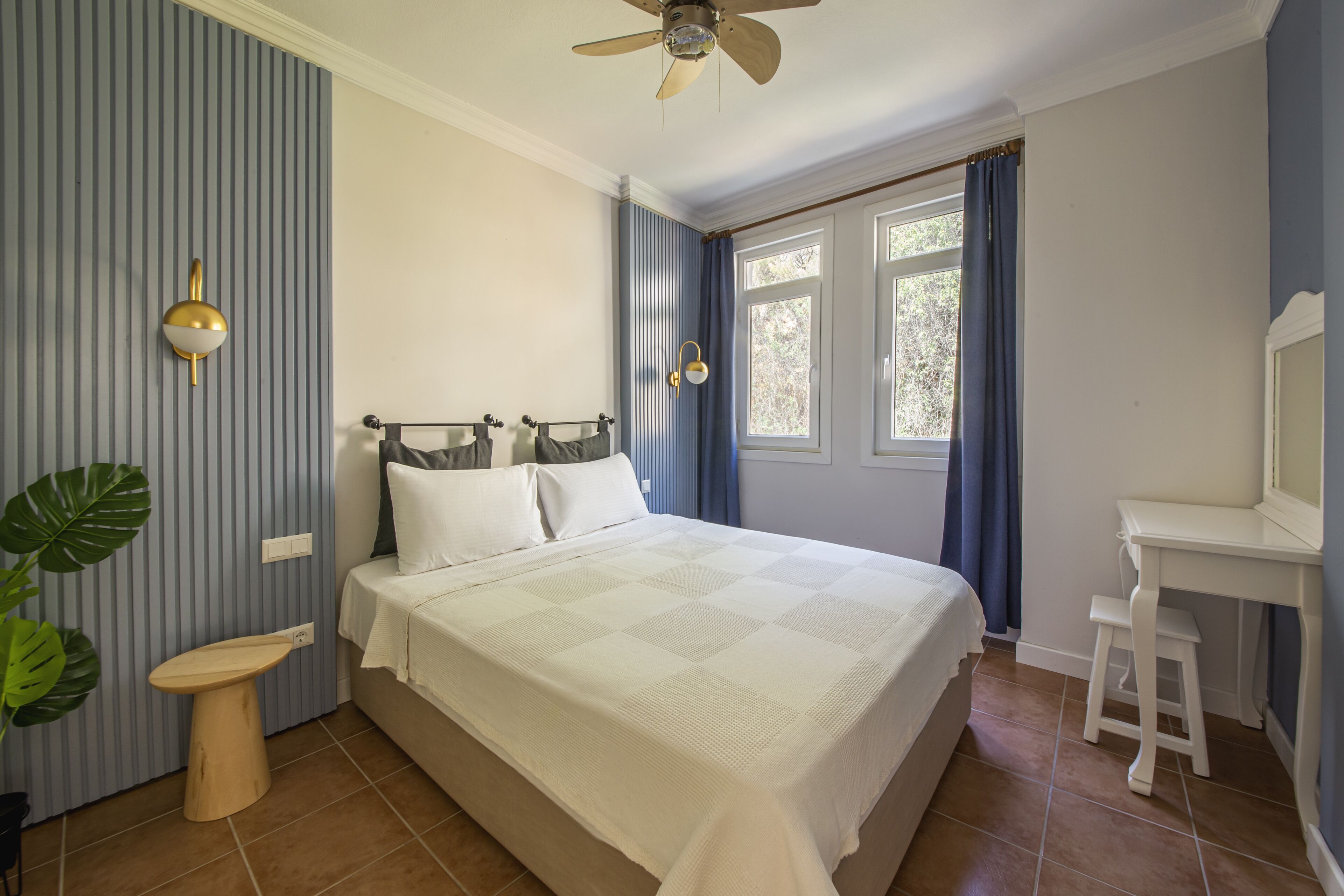 Ein Schlafzimmer mit Bett, Schreibtisch, Stuhl, Deckenventilator und einem Fenster mit Vorhängen.