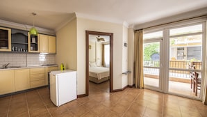 Cocina compacta con refrigerador, alacenas y lavamanos. Hay un balcón con vistas al exterior.
