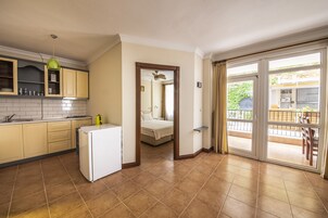Cocina compacta con refrigerador, alacenas y lavamanos. Hay un balcón con vistas al exterior.