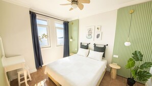 Un dormitorio con cama, escritorio, silla, ventilador de techo y ventana con cortinas.