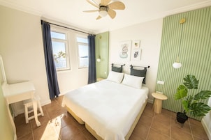 Un dormitorio con cama, escritorio, silla, ventilador de techo y ventana con cortinas.
