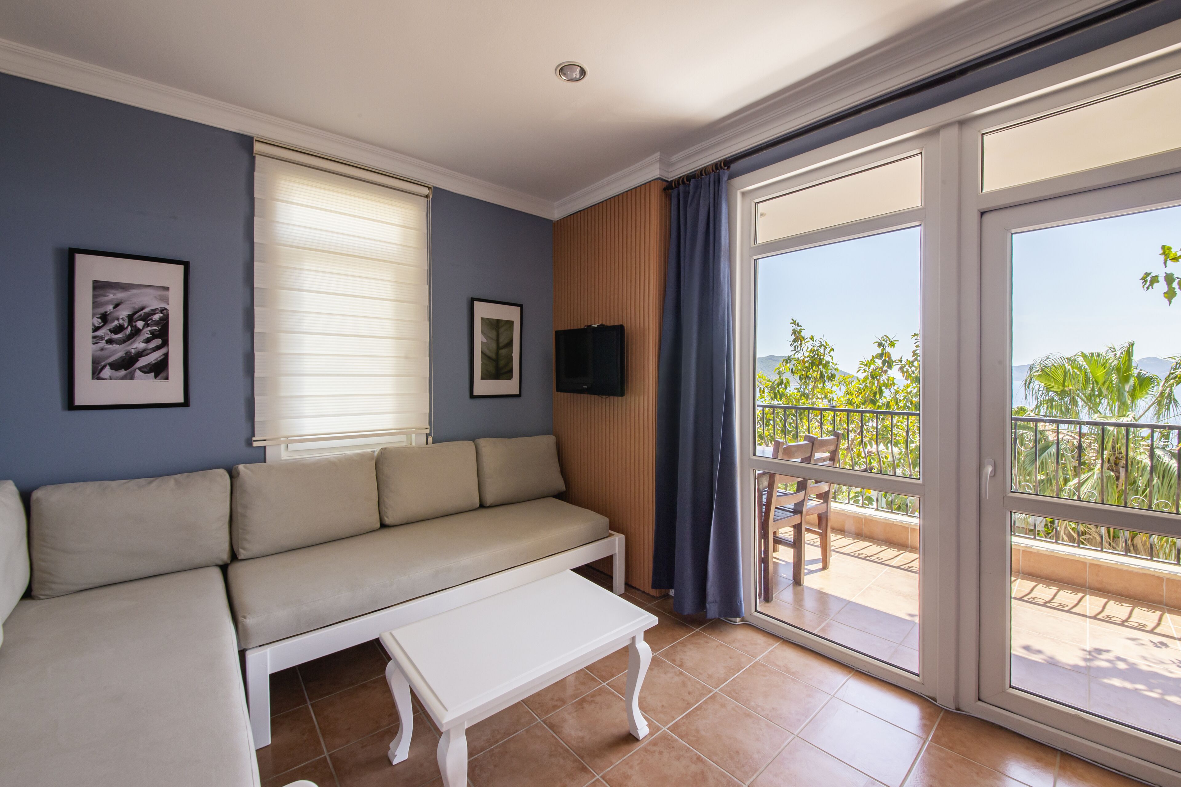 Un salon comprenant un canapé, une table basse, un téléviseur et un balcon offrant une vue sur la verdure et les montagnes.