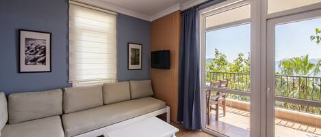 Un salon comprenant un canapé, une table basse, un téléviseur et un balcon offrant une vue sur la verdure et les montagnes.