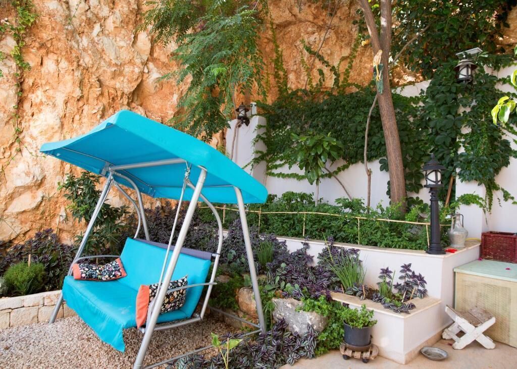 A garden with a swing chair, potted plants, and a rustic wall.