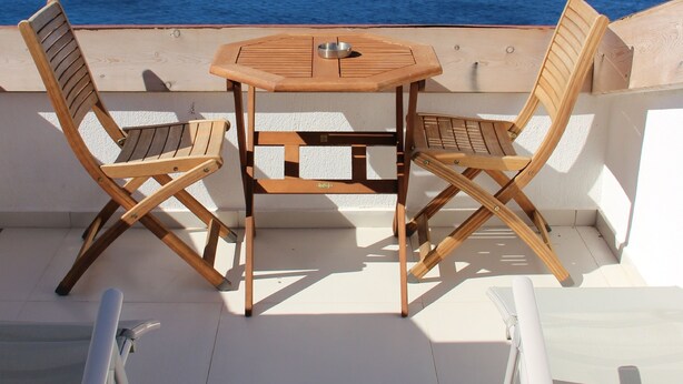 Una mesa y sillas de madera en un balcón con vista al mar y a islas distantes.