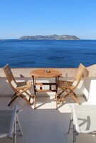Una mesa y sillas de madera en un balcón con vista al mar y a islas distantes.