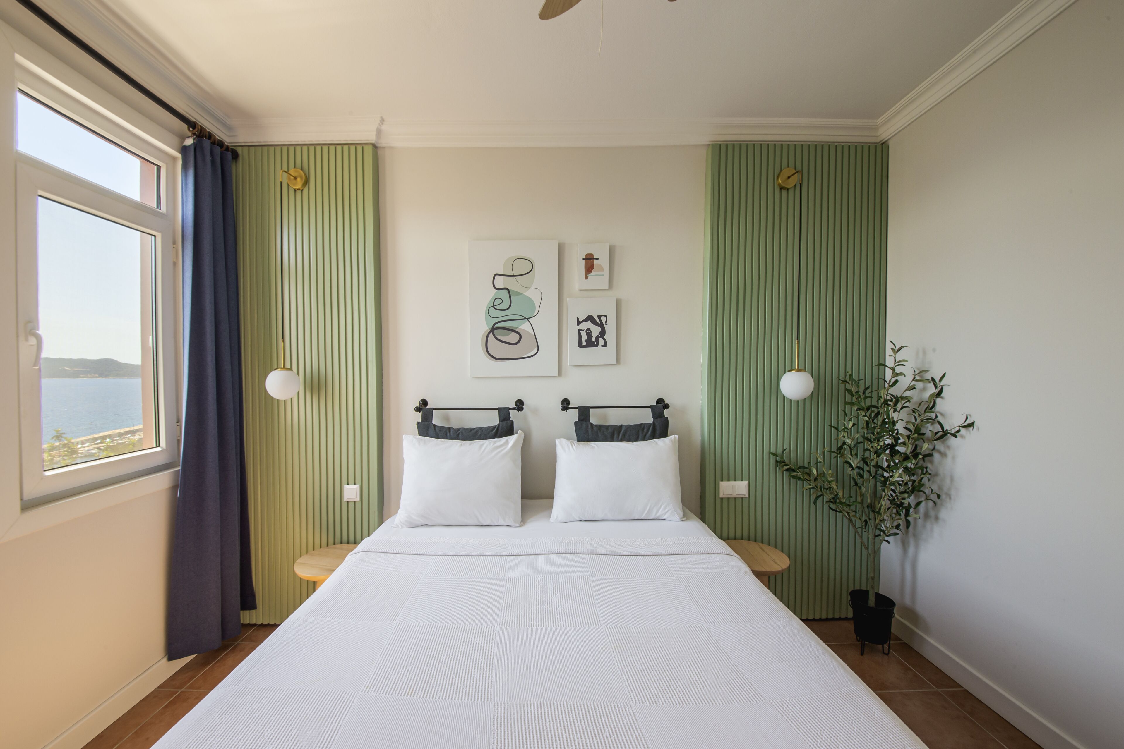 A neatly arranged bedroom with a large bed, two bedside tables, a potted plant, and artwork on the wall.