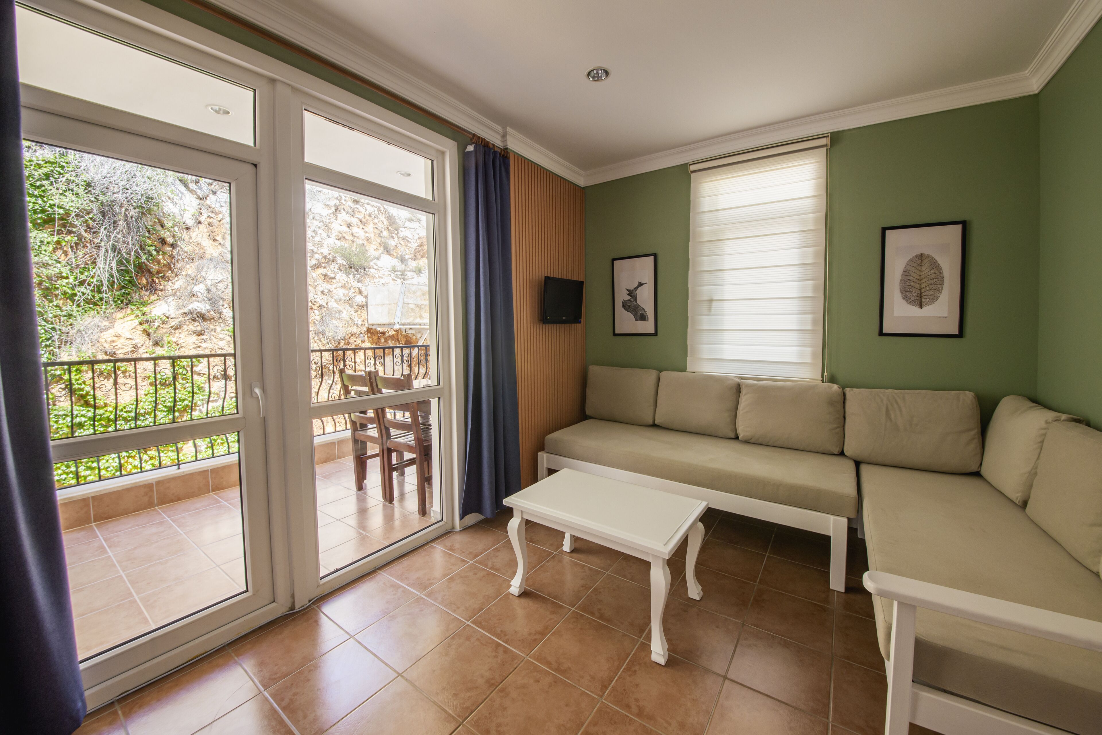 Sala de estar con sofá, mesa de centro y televisor. Hay una puerta corrediza de vidrio que da a un espacio exterior con mesa y sillas.
