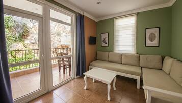Sala de estar con sofá, mesa de centro y televisor. Hay una puerta corrediza de vidrio que da a un espacio exterior con mesa y sillas.