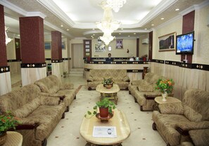 A lobby with patterned sofas, a reception desk, a chandelier, and a television.