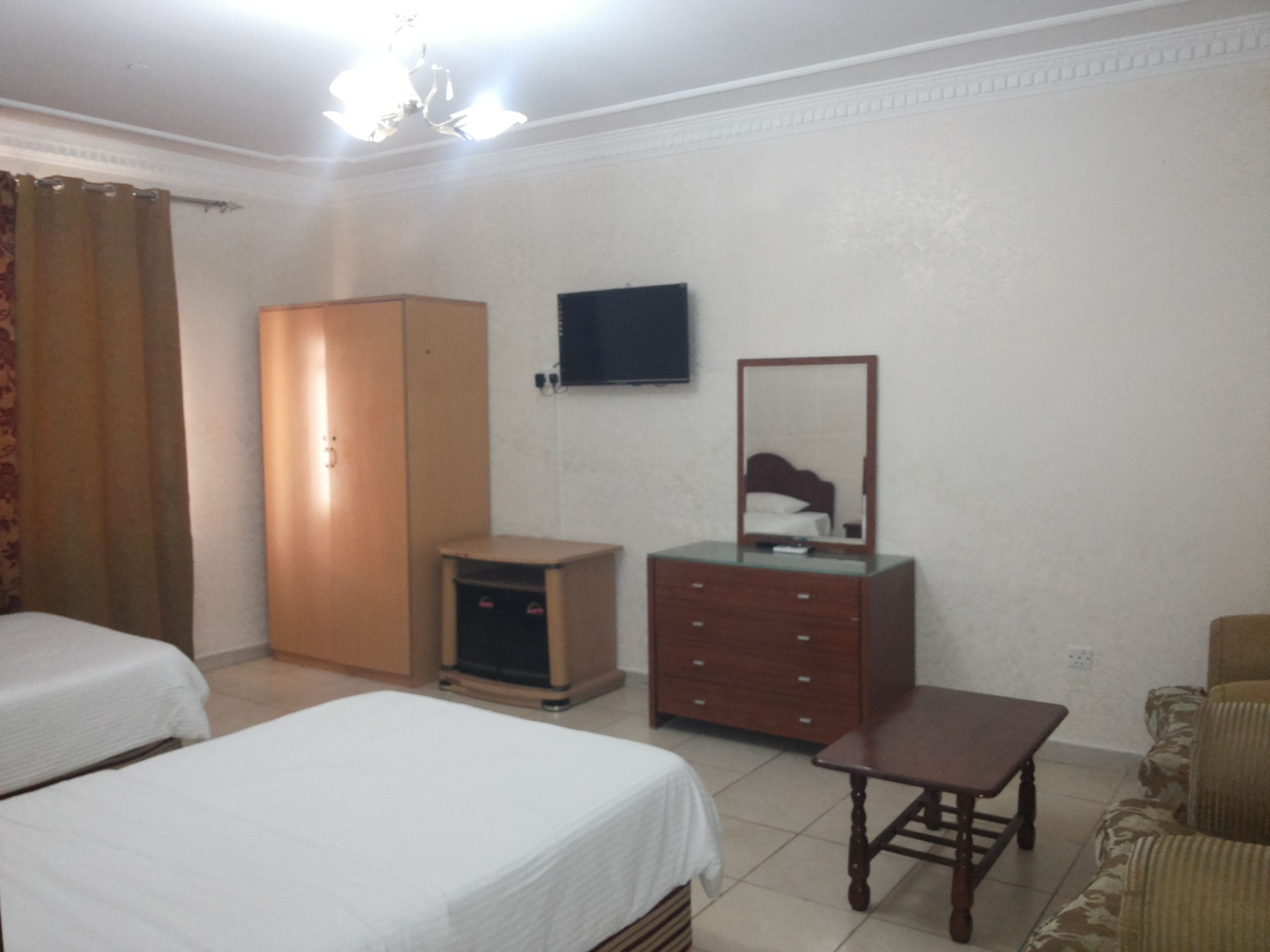 A hotel room with two beds, a wardrobe, a television, a mirror, a small table, and a sofa.