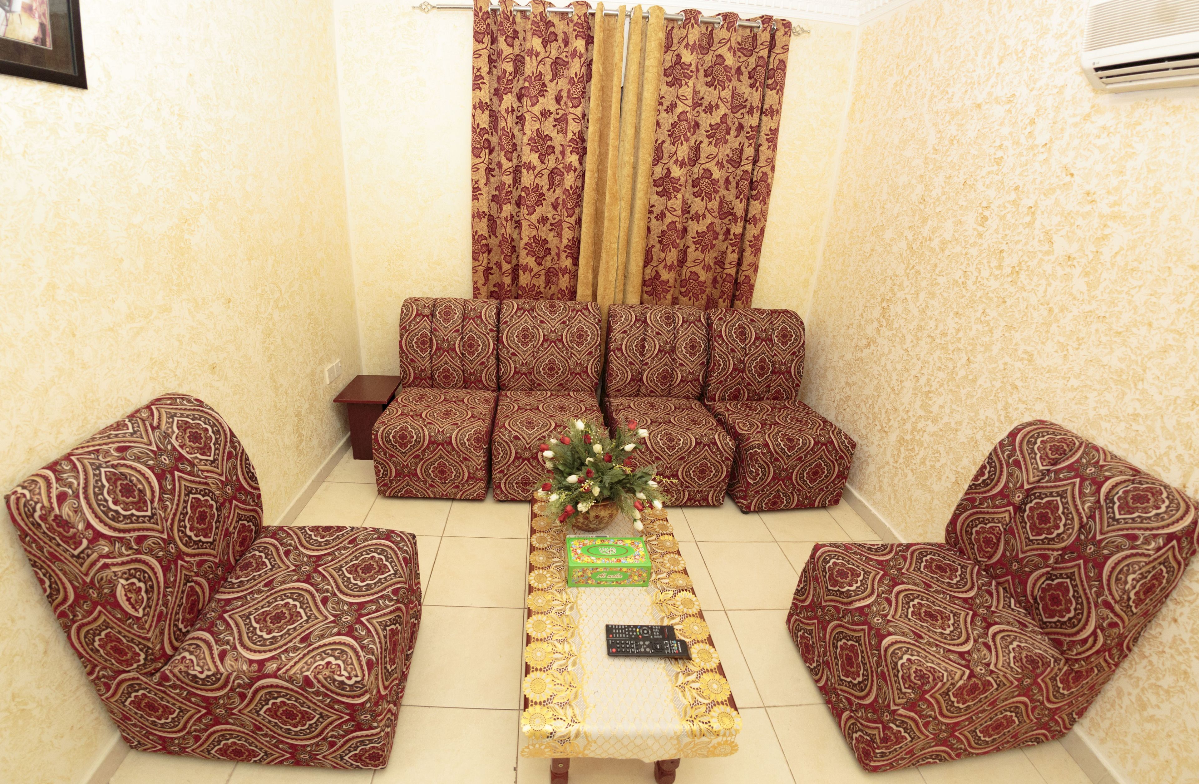 Uma sala de estar com sofás estampados, uma mesa de centro com controle remoto e uma planta decorativa.