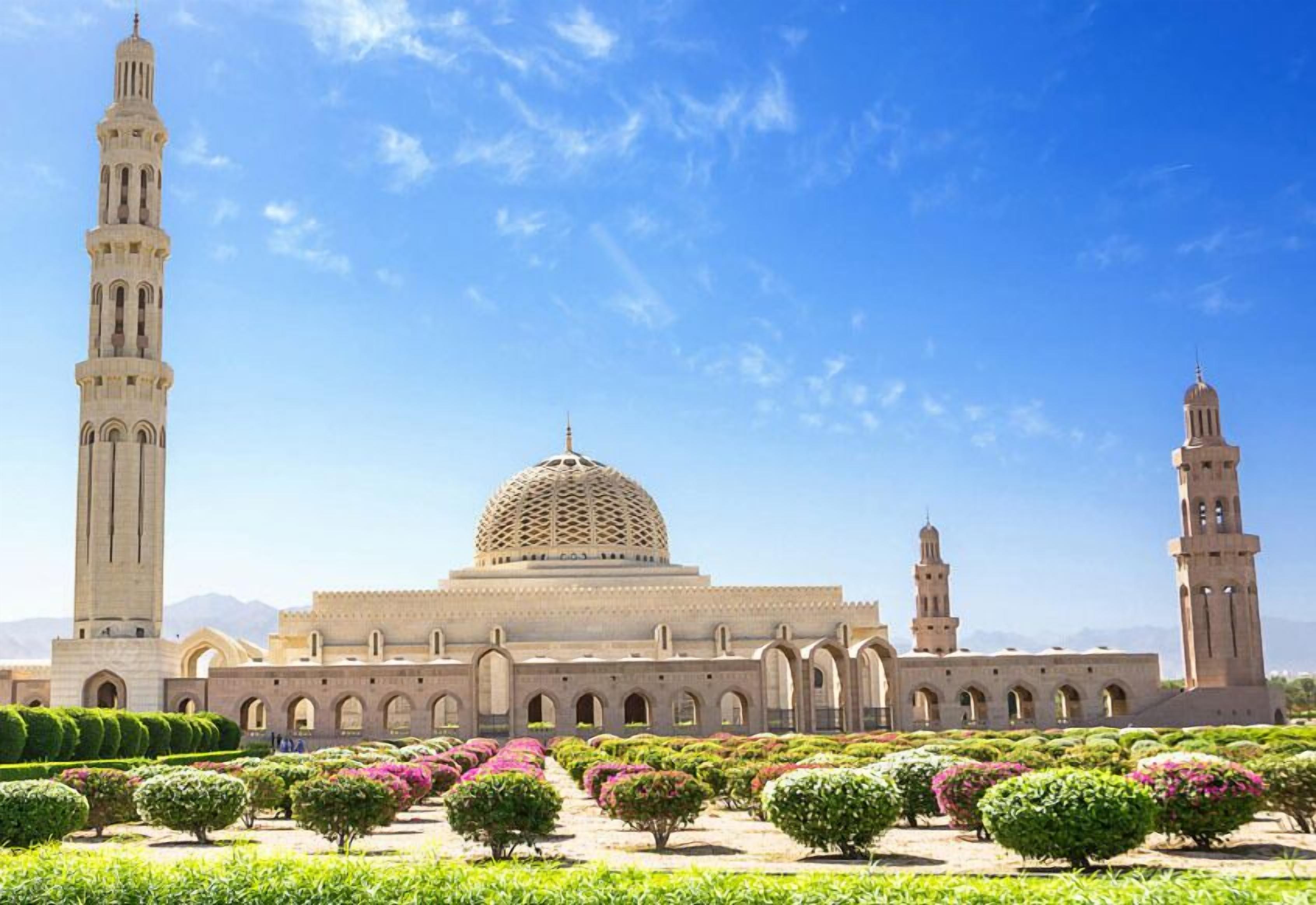 Una gran mezquita con una cúpula destacada y altos minaretes, rodeada de jardines cuidados.