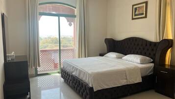 A bedroom with a large bed, a nightstand, a dresser, and a view of a balcony.