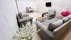 Uma sala de estar moderna com sofás cinzas, uma mesa de centro de vidro e uma área de jantar ao fundo.