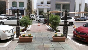 Vista da rua com área de estacionamento, plantas em vasos e um edifício com uma placa que diz 'COPPA CAFE'.