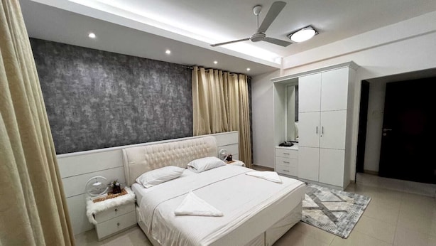 Quarto moderno com cama grande, guarda-roupa, mesa de cabeceira e ventoinha no teto.