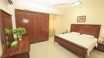 A bedroom with a bed, a wardrobe, a desk with a vase of flowers, and a ceiling fan.