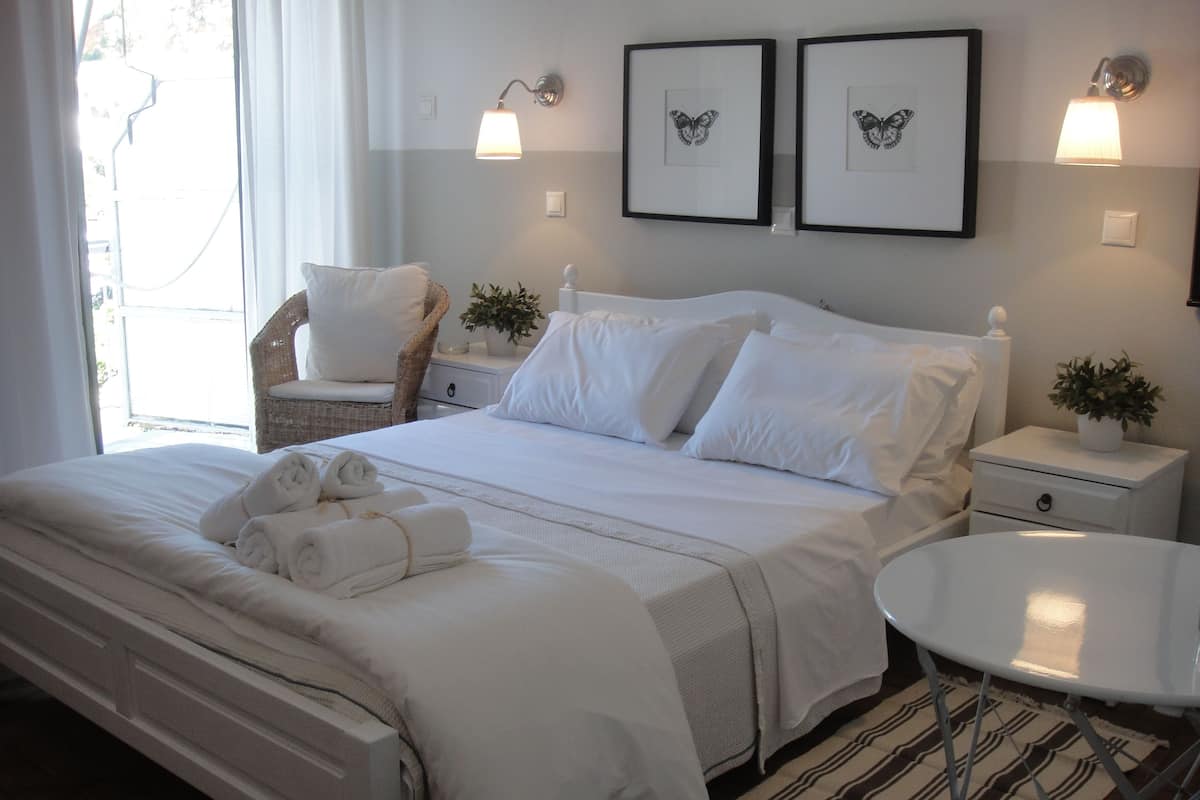 A neatly made bed with white linens and towels, a bedside table with a lamp, a chair, and two framed butterfly artworks on the wall.