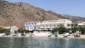 Ein Hotel an der Küste mit mehreren Etagen, Außenbestuhlung und Blick auf Meer und Hügel.