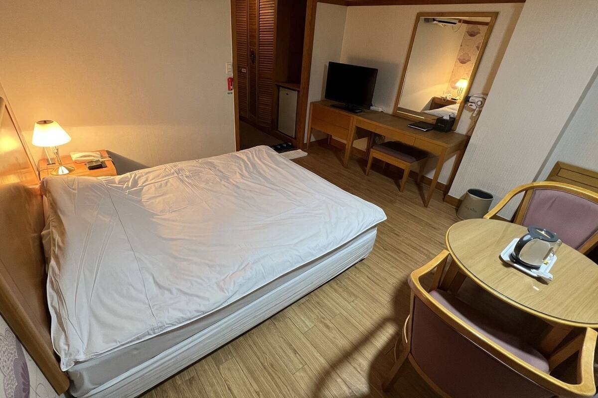 A hotel room with a bed, a desk with a chair, a TV, and a mirror.